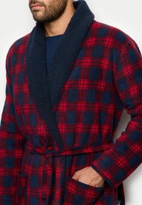 Rot und marineblau karierter Bademantel aus weichem, strukturiertem Stoff. Mit Schalkragen, Gürtel und Fronttaschen.