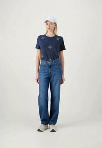 Navy t-shirt with star prints, paired with loose blue denim jeans. White cap and light sneakers complete the look.