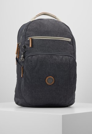 Sac à dos en tissu gris foncé avec deux poches zippées, tirettes en cuir, un logo circulaire et un petit porte-clés sur une surface blanche.