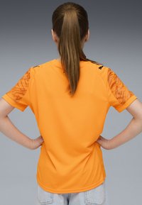 Maglietta sportiva arancione a maniche corte con maniche testurizzate a motivo, parte anteriore liscia e dettagli neri sulle spalle.