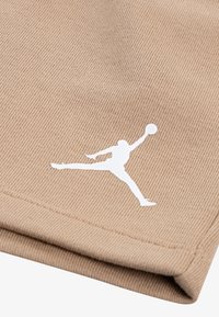 Beiger Stoff mit strukturierter Strickerei, auf der Oberfläche ist eine weiße Silhouette eines springenden Athleten aufgedruckt. Kantennaht sichtbar.