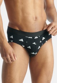 Schwarze Slips mit geometrischem weißen Muster. Das Material scheint weich zu sein, mit einer engen Passform und einem nahtlosen Bund.