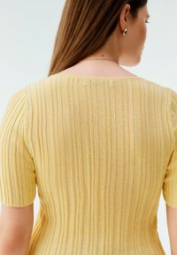 Gul ribbad stickad topp med korta ärmar, som har en rundad halsringning och texturerade tygdetaljer.