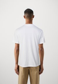 T-shirt en coton blanc avec un col rond, des manches courtes et une coupe décontractée. Texture lisse et design simple ; sans logos ni motifs visibles.