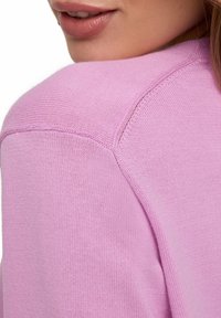 Maglioncino rosa chiaro lavorato a maglia con una vista ravvicinata della cucitura della spalla, che mette in evidenza la trama a coste e i dettagli di rifinitura curati.