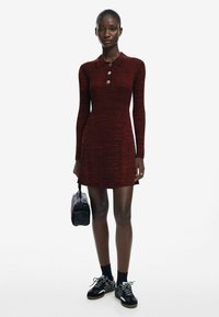 Abito lavorato a maglia rosso con maniche lunghe, colletto e dettagli con bottoni. Accompagnato da una piccola borsa nera e sneakers nere con accenti bianchi.