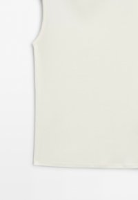 Close-up of the bottom half of a plain, light beige sleeveless top with a smooth texture on a white background.