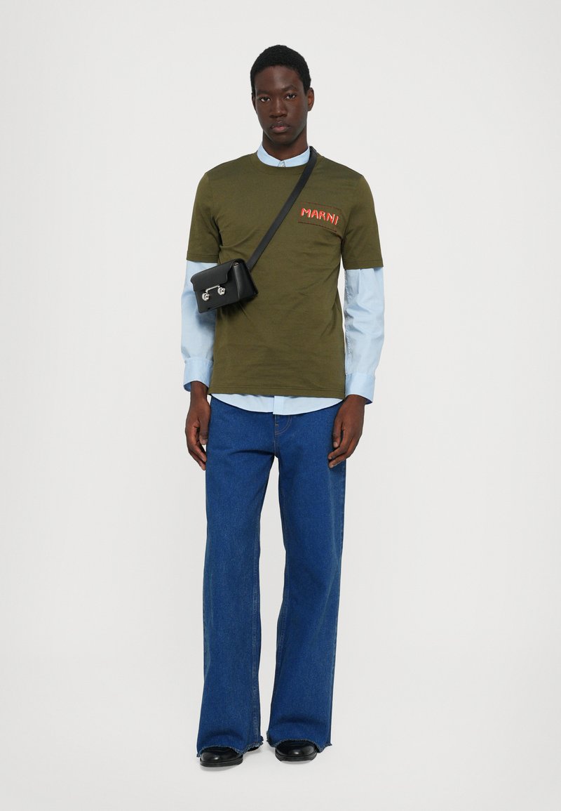 Camiseta verde oliva con logo rojo "MARNI", superpuesta a una camisa de cuello azul claro, combinada con unos jeans de campana azul oscuro y un bolso cruzado negro.