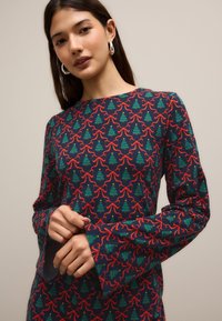 Robe à manches longues en tissu bleu marine avec un motif d'arbres de Noël verts et de nœuds rouges, dotée de poignets de manches évasés.