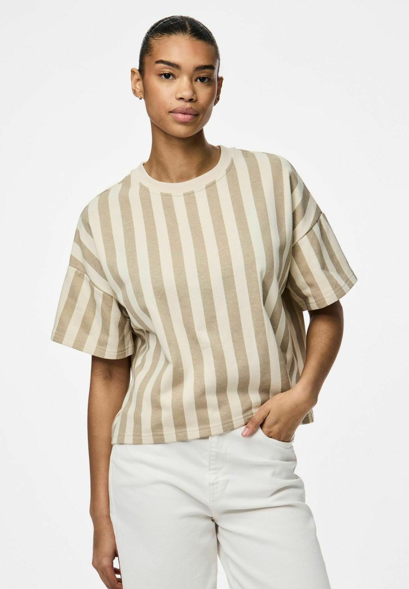 T-shirt a righe beige con una vestibilità comoda e maniche corte, realizzato in morbido cotone. Abbinato a pantaloni chiari.