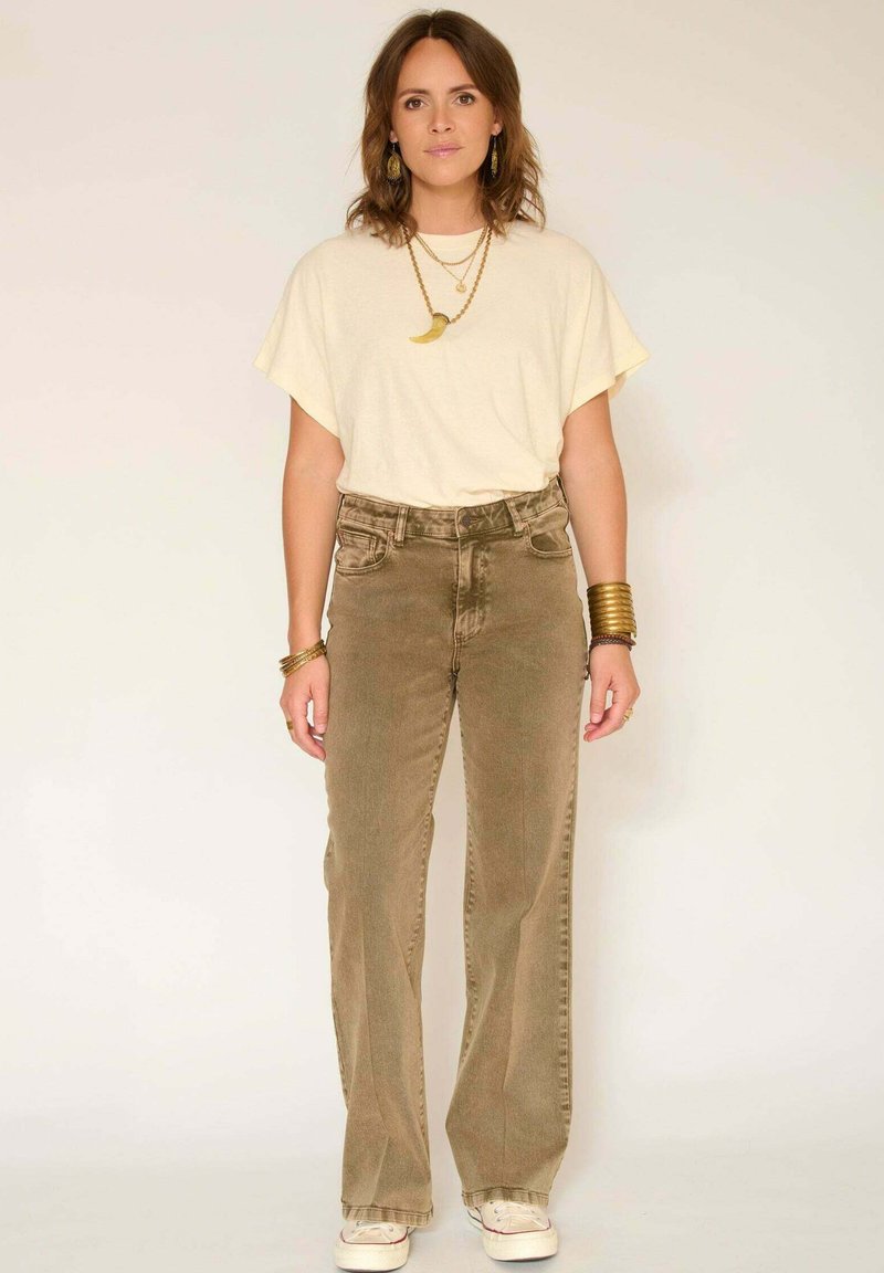 T-shirt beige oversize, pantalon en velours côtelé vert olive taille haute avec jambes droites, et baskets blanches avec des accents rouges.