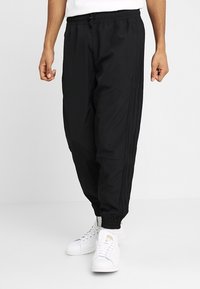 Svarta joggerbyxor med elastisk midja och sidostreck. Tillverkade av lätt tyg, med muddade anklar och sidfickor.