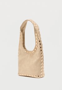 Sac beige de forme hobo, avec une large bandoulière et des clous circulaires le long des bords. Fabriqué en matériau lisse, couleur unie, sans motifs.