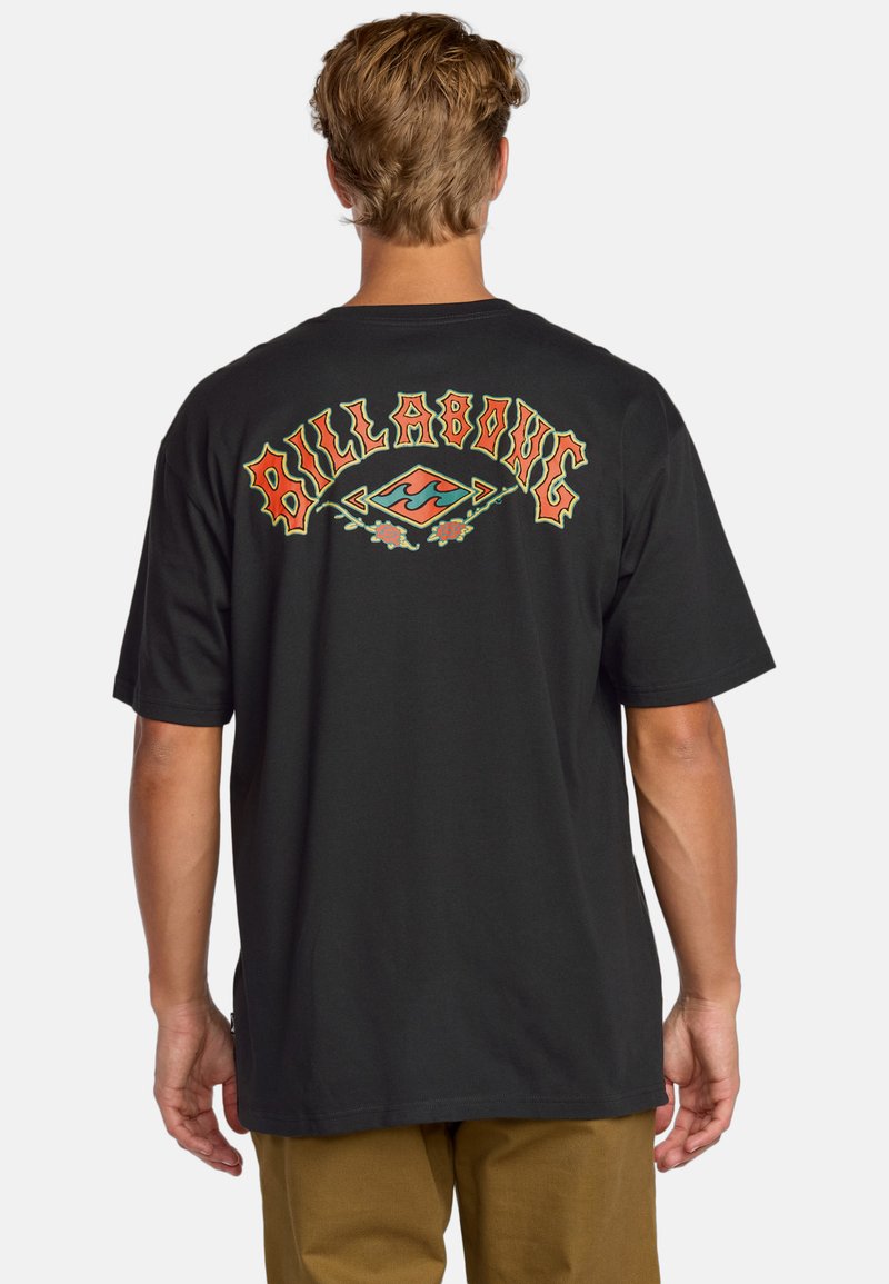 Camiseta negra con el texto colorido "Billabong" acompañado de acentos florales y un gráfico de olas en la parte trasera. Manga corta, ajuste estándar.