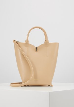 Beige leather handbag with rounded handles and a long strap, standing on a white surface against a plain light gray background.