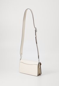 Weiße Lederhandtasche mit einer glatten Textur, einem geschwungenen oberen Rand, einem abnehmbaren Tragegurt und silbernen Hardware-Akzenten.