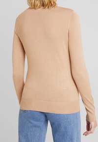 Ljusbeige tröja med långa ärmar, ribbad fåll och mjuk textur. Buren med blå denimjeans som har en slät, figurnära design.