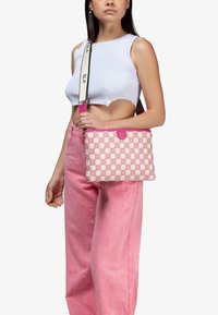 Borsa a tracolla rosa con motivo geometrico, tessuto liscio e tracolla removibile. Presenta un accento rosa sulla parte superiore.