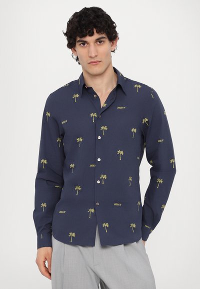 Camicia blu navy con ricamo di palme gialle e testo "DREAM". Maniche lunghe con bottoni, vestibilità strutturata e orlo curvo.