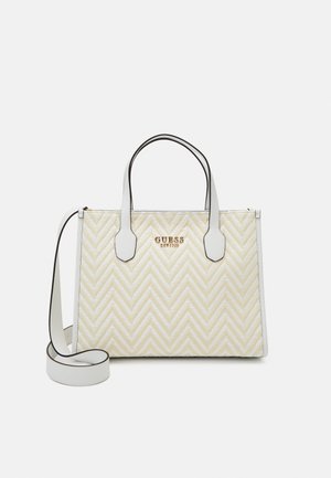 Cremeweiße Guess-Handtasche mit Chevron-Muster, zwei Griffen und abnehmbarem Schulterriemen auf einfarbigem Hintergrund.
