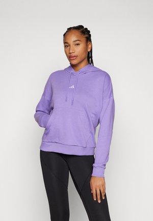 Violet stilingas megztinis su priekiu kišene, su kapuce ir Adidas logotipu; pasižymi minkšta medžiaga ir laisvu siluetu; derinamas su juodomis antblauzdžiais.