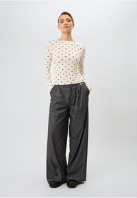 Ilgs piedurkņu krēms tops ar melniem punktiņiem, apvienots ar pelēkiem svītrains plašiem biksēm, valkāts ar melnām kurpēm. Minimālistisks dizains.