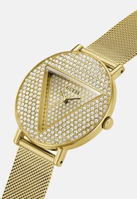 Guldur med en meshrem, der har en rund urskive prydet med en trekant af klare rhinsten og en enkel urskive med time- og minutvisere.