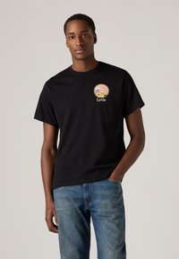 Tricou din bumbac negru cu mâneci scurte, având un imprimeu grafic circular în roz și galben pe piept, etichetat "Levis".