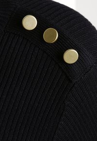 Tissu en maille marine avec nervures verticales. Trois boutons ronds en or le long du bord. Texture douce, vue en gros plan.