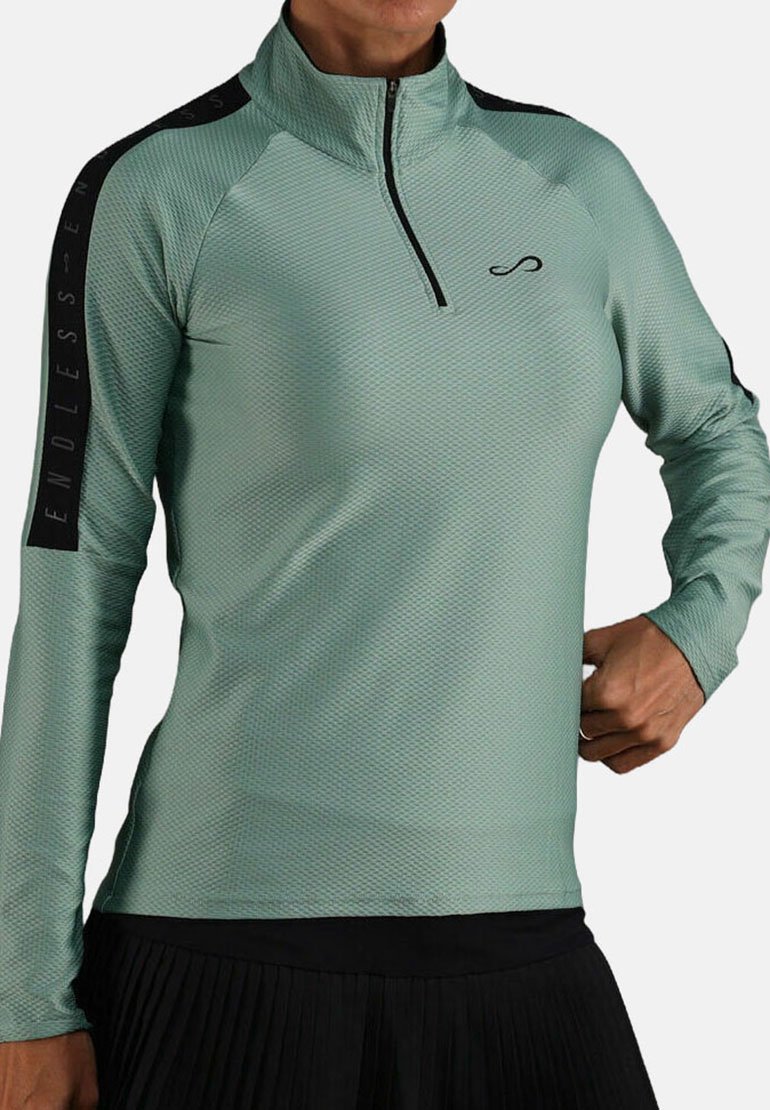 Langzaam, mintgroen sporttop met lange mouwen en een hoge kraag en een kwart rits. Heeft een textuurstof en zwarte accentdetails op de mouwen.