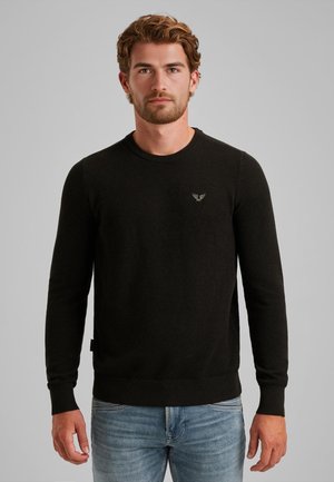 Schwarzer Strickpullover mit rundem Halsausschnitt, langen Ärmeln, gerippten Abschlüssen und einem kleinen Emblem auf der Brust. Weiche Textur, taillierter Schnitt.