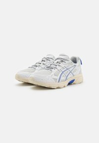 Baskets blanches avec accents bleus, en mesh et matériau synthétique, semelle texturée et design à lacets. Présente un logo de marque distinctif.