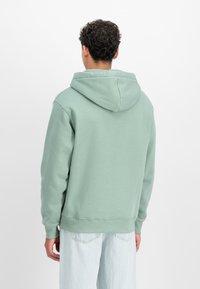 Menta zöld kapucnis pulóver kenguruzsebbekkel, bordás mandzsettákkal és aljjal, valamint bélelt kapucnival. Világoskék, kényelmes szabású farmernadrággal viselve.