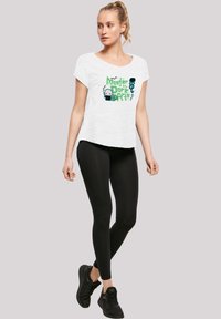 Hvit T-skjorte med grafisk trykk som har tekst og karakterer, parret med svarte leggings og svarte joggesko. Casual passform, kortermet.