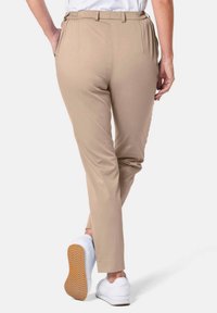 Beige op maat gemaakte broek met elastische taille en zijzakken, taps toelopend ontwerp, gecombineerd met witte sneakers. Zachte textuur en geen zichtbare patronen.