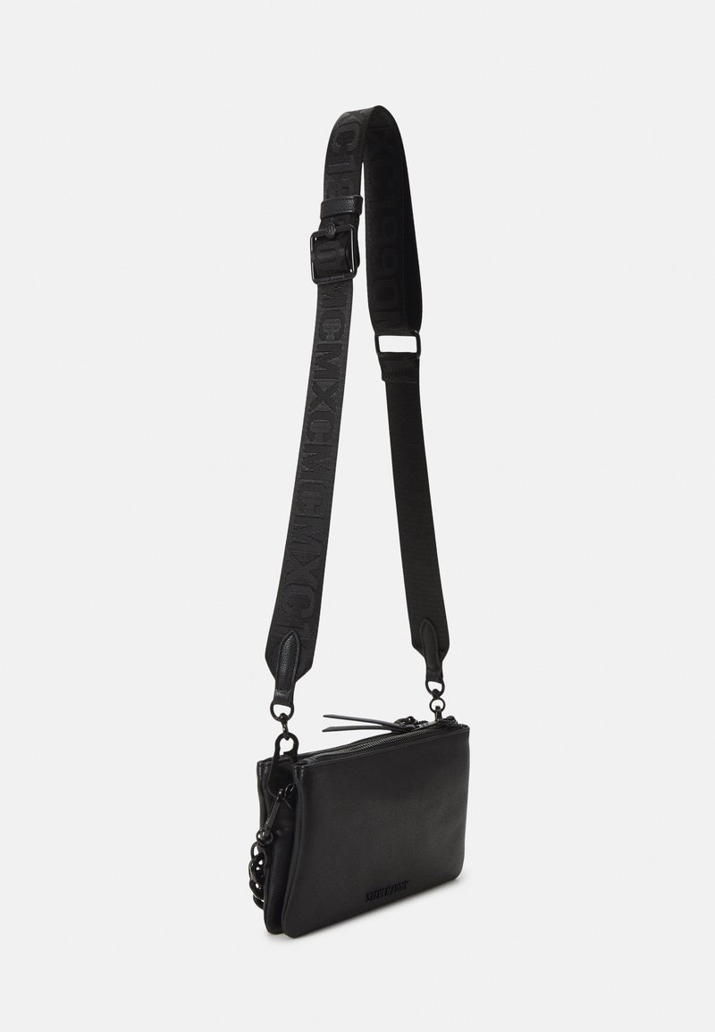 Sac bandoulière en cuir noir avec une large sangle réglable présentant un texte embossé et une fermeture éclair sur un fond uni.
