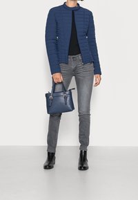 Giacca trapuntata blu navy con colletto alto, jeans grigi slim, stivaletti neri alla caviglia e una piccola borsa blu navy con dettagli in oro.