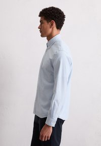 Camisa de manga larga a rayas azul claro, hecha de algodón. Presenta un collar abotonado, un bolsillo en el frente y puños abotonados. Diseño de corte entallado.