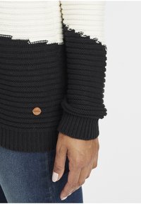 Svart og kremfarget strikkegenser med teksturerte striper, med en råkantdesign, ribbestrikkede mansjetter og en liten trelogo-detalj.