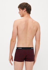 Bóxer en negro con un patrón de cuadrícula roja; cuenta con una cinturilla suave con el logo "HUGO"; diseño ajustado, textura textil suave.