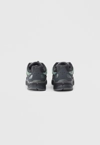 Black athletic shoes with a textured mesh upper and green accents, featuring a thick sole and molded details on the heel.