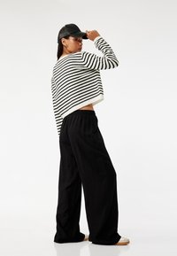 Gestreepte gebreide trui in zwart-wit, cropped ontwerp, gecombineerd met losse zwarte broek en een zwarte pet. Glad textuur, casual fit.