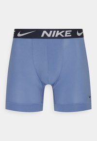Nike plave bokserice s crnim pojasom na kojem se nalazi bijeli "NIKE" branding. Izrađene su od glatkog materijala, imaju prilagođen dizajn i dođu do sredine bedara.