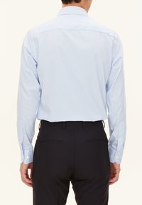 Camicia azzurro chiaro a maniche lunghe con sottili righe verticali, polsini abbottonati e colletto classico, abbinata a pantaloni scuri su misura.