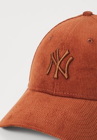 Oranžinė kordūrinė beisbolo kepurė, kuriuose priekyje yra rudas išsiuvinėtas NY logotipas. Skydelis plokščias su tekstūruota apdaila.