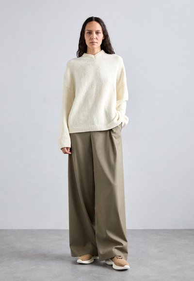 Maglione crema a maglia con collo alto, abbinato a pantaloni larghi color verde oliva. Le calzature consistono in sneakers beige.