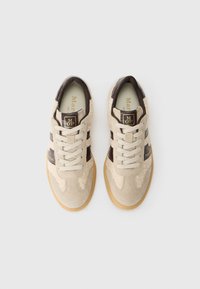 Sneaker in suede beige con dettagli in pelle marrone, punta arrotondata, lacci piatti e un pannello laterale testurizzato e morbido. Suola in gomma marrone.