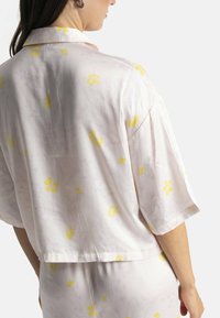 Haut à manches courtes, rose pâle avec motifs floraux en tissu léger ; présente des motifs de fleurs jaunes et subtils en lavande ; coupe décontractée et ourlet court.