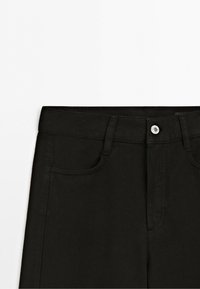 Sort denim bukser talje sektion med bæltestropper, metal knaplukning og forlommer på hvid baggrund.