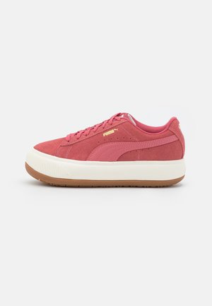 Sneaker basse Puma en daim rose avec une semelle blanche épaisse, une semelle extérieure en caoutchouc, un détail de bande rose et des lacets roses sur un fond neutre.
